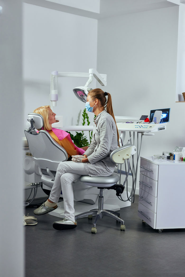 dentist-in-mask-and-patient-sitting-in-dental-chair-talking-about-treatment